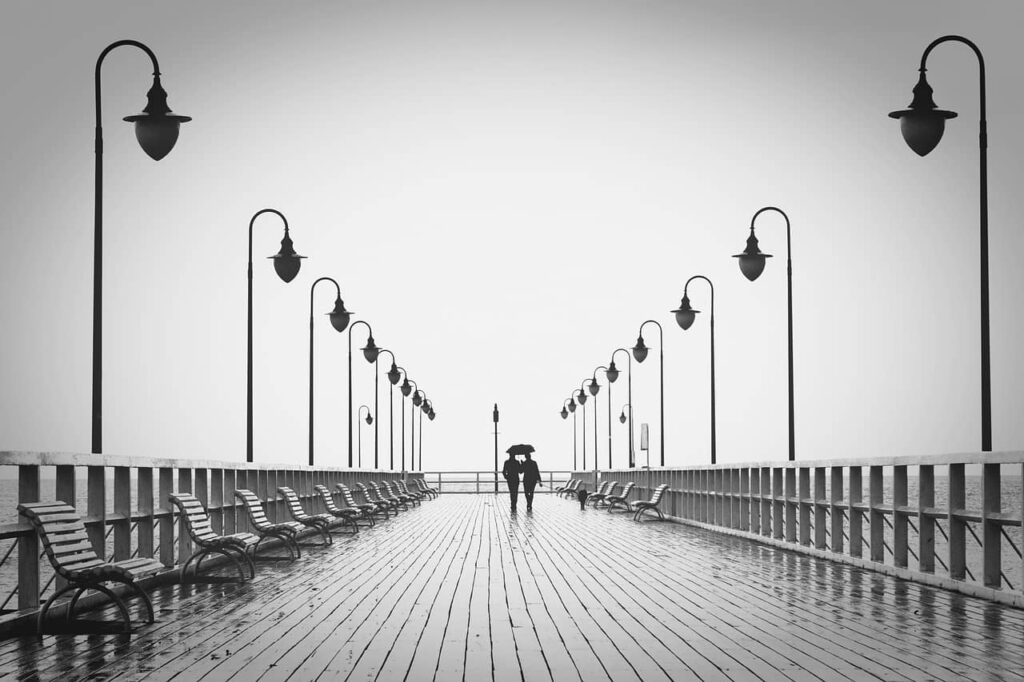 Personas alejándose en un muelle bajo la lluvia, símbolo del duelo por ruptura que tratamos con terapia individual en Marbella.
