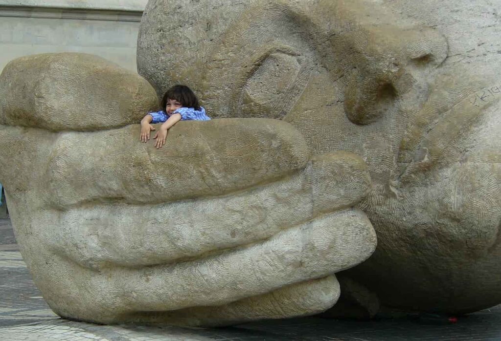 Escultura gigante de piedra tapándose la boca con la mano, simbolizando la invalidación emocional que abordamos en terapia psicológica en Marbella.